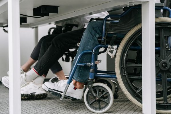 unter einem Schultisch sieht man, dass Schüler*innen sowohl auf Stühlen als auch im Rollstuhl sitzen